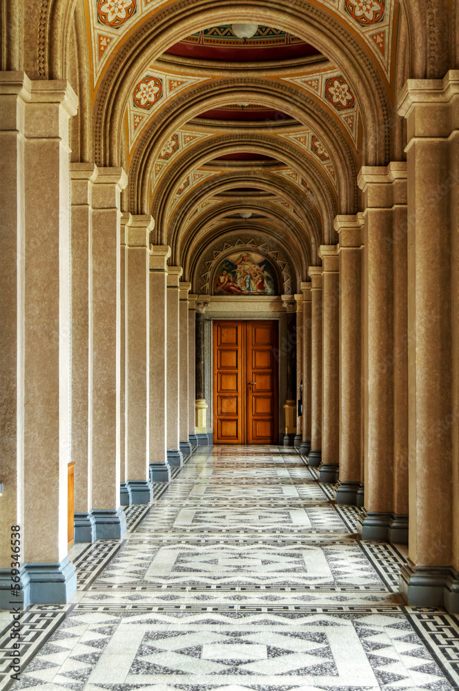A corridor of white columns and high ceilings, with a door at the end. Architecture, old