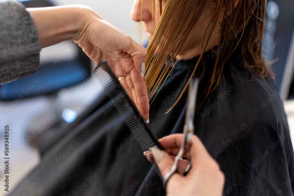Naklejka premium Unrecognizable hairdresser using scissors and comb to cut hair of anonymous client in salon