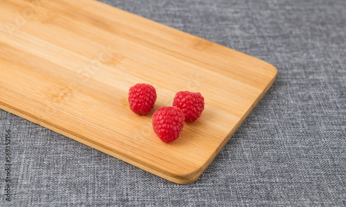 Three raspberries on a wooden cutting board on a crey background photo