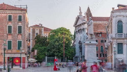 Tourists walking around the monument of Niccolo Tommaseo timelapse on the Campo Santo Stefano city square. Clear summer sky before sunset. Venice, Italy photo