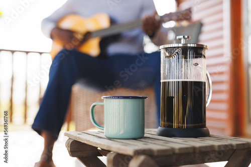 French press and mug on table over midsection of african american senior man playing guitar photo