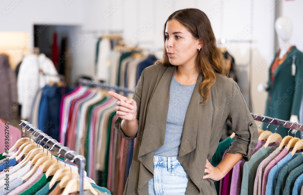 Young cheerful positive female shopper examining warm sweaters in women cloths shop