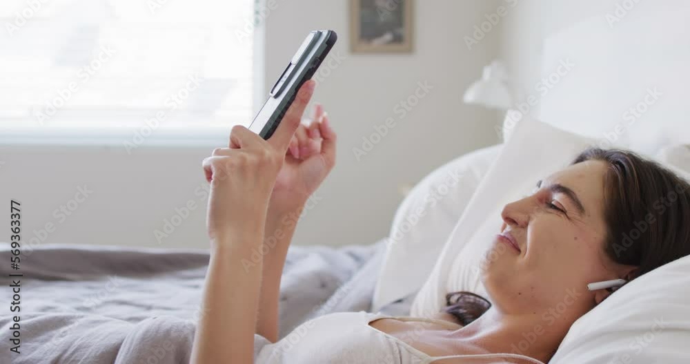Happy caucasian woman relaxing, lying in bed and using smartphone Happy caucasian woman relaxing, lying in bed and using smartphone