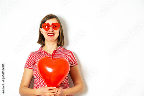 Portrait of the beautiful smiling woman in red sunglasses holding in her hand a red heart balloon for Valentines Day.