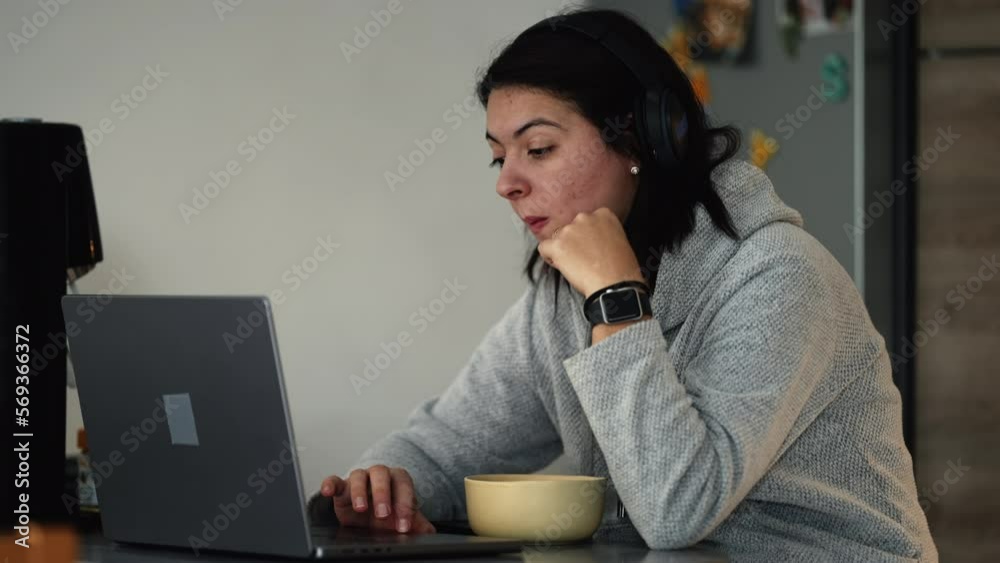 Candid woman browsing internet in front of laptop computer working at home kitchen