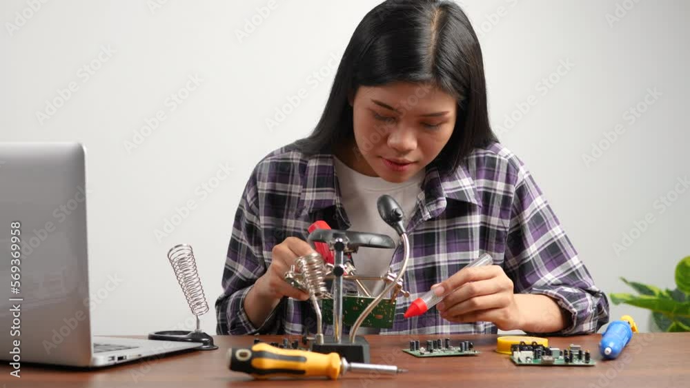 4K: Young Asian woman technician uses a soldering iron to repair circuit board on work table. 4K: Young Asian woman technician uses a soldering iron to repair circuit board on work table.