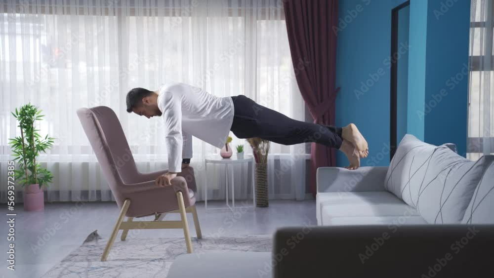 Sportsman doing pushups briskly using sofa and armchair. Young athlete