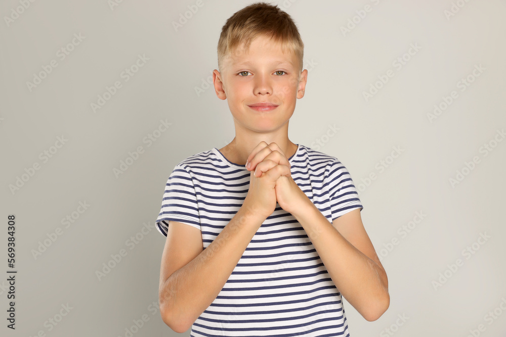 Boy with clasped hands praying on light grey background Boy with clasped hands praying on light grey background
