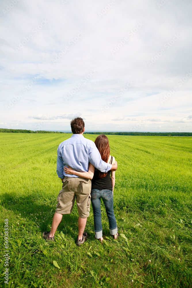 Rear view of young couple hugging and overlooking farmland.