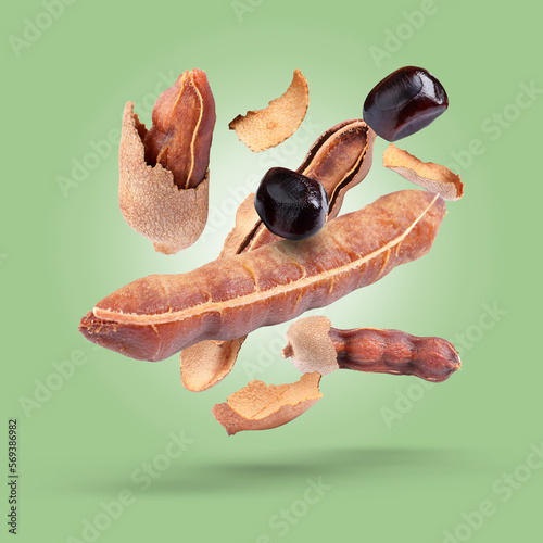 Ripe tamarind pods and seeds falling on light green background
