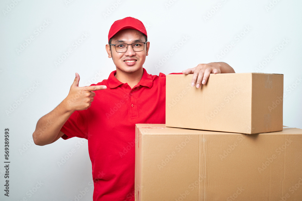 Confident asian courier man in red uniform encourage call service, showing and pointing at cardboard box while lean on it Confident asian courier man in red uniform encourage call service, showing and pointing at cardboard box while lean on it