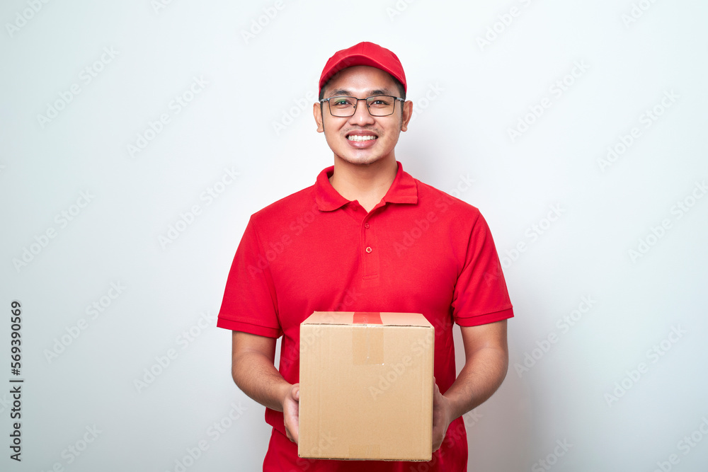 Asian young courier man wearing red cap and tshirt standing over isolated white background holding cardboard boxes in front Asian young courier man wearing red cap and tshirt standing over isolated white background holding cardboard boxes in front