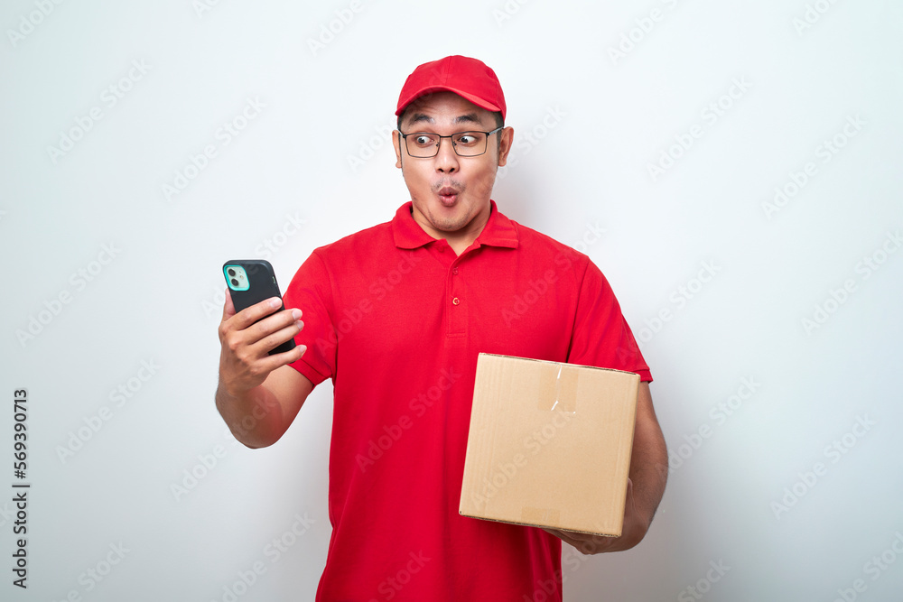 Asian courier man in red uniform smiling look at his smartphone while holding cardboard box parcel Asian courier man in red uniform smiling look at his smartphone while holding cardboard box parcel