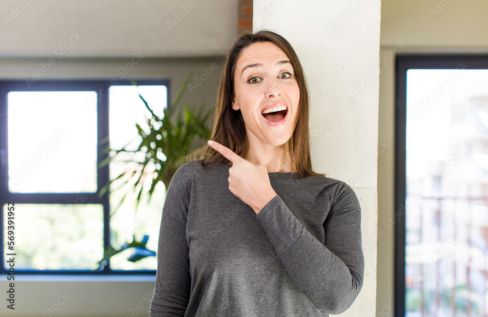 young adult pretty woman looking excited and surprised pointing to the side and upwards to copy space young adult pretty woman looking excited and surprised pointing to the side and upwards to copy space