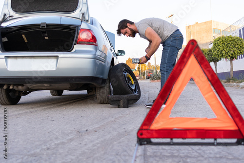 young man changing a flat tire on the road, using a hazard triangle