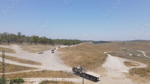 Israel Army infantry squad soldiers on vehicles driving through green field at training ground country road, Aerial Tracking shot photo