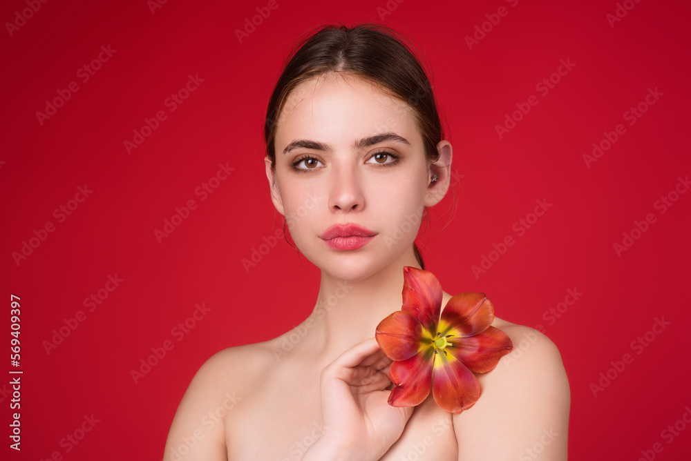 Beauty and flower. Youth and skin care concept. Sensual girl with tulip near naked shoulder. Beautiful sensual woman hold tulips, studio portrait on red background. Beauty and flower. Youth and skin care concept. Sensual girl with tulip near naked shoulder. Beautiful sensual woman hold tulips, studio portrait on red background.