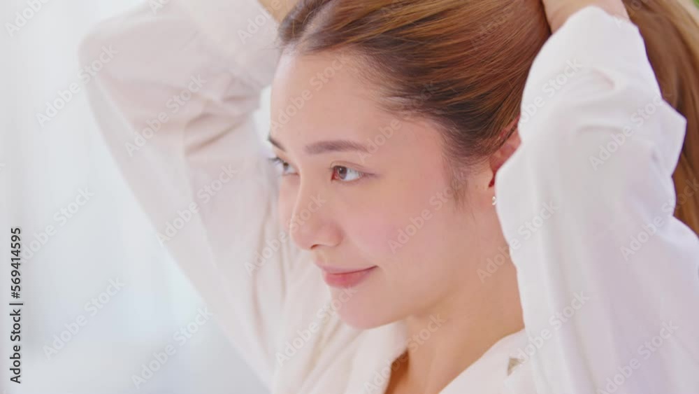 Beautiful Asian young woman tie the hair back before shower or apply cream or lotion on face. Beauty female grab her hairs after wake up with happiness and positive emotional. Self care concept Beautiful Asian young woman tie the hair back before shower or apply cream or lotion on face. Beauty female grab her hairs after wake up with happiness and positive emotional. Self care concept