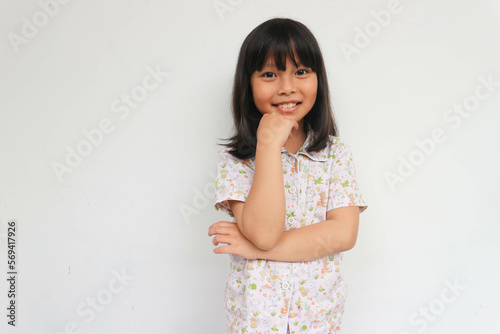 Beautiful kid girl with straight hair wearing pajama looking confident at the camera with smile with crossed arms and hand raised on chin. thinking positive.