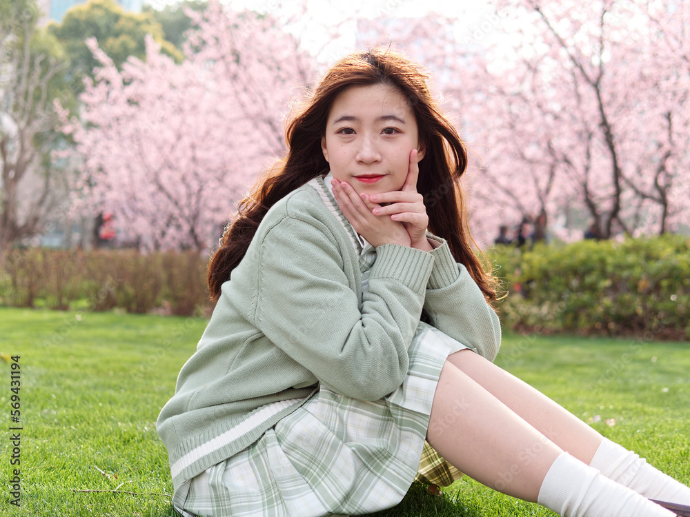 Outdoor portrait of beautiful young Chinese girl in Japanese JK style dress sitting with blossom cherry tree brunch background in spring garden, beauty, summer, emotion, expression and people concept. Outdoor portrait of beautiful young Chinese girl in Japanese JK style dress sitting with blossom cherry tree brunch background in spring garden, beauty, summer, emotion, expression and people concept.