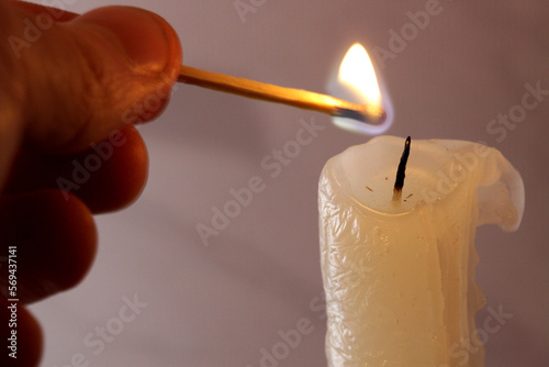 A hand with a burning match lights a candle.