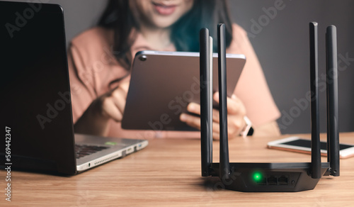 Selective focus at router. Internet router on working table with blurred happy woman using tablet at the background. Fast and high speed internet connection from fiber line with LAN cable connection. photo