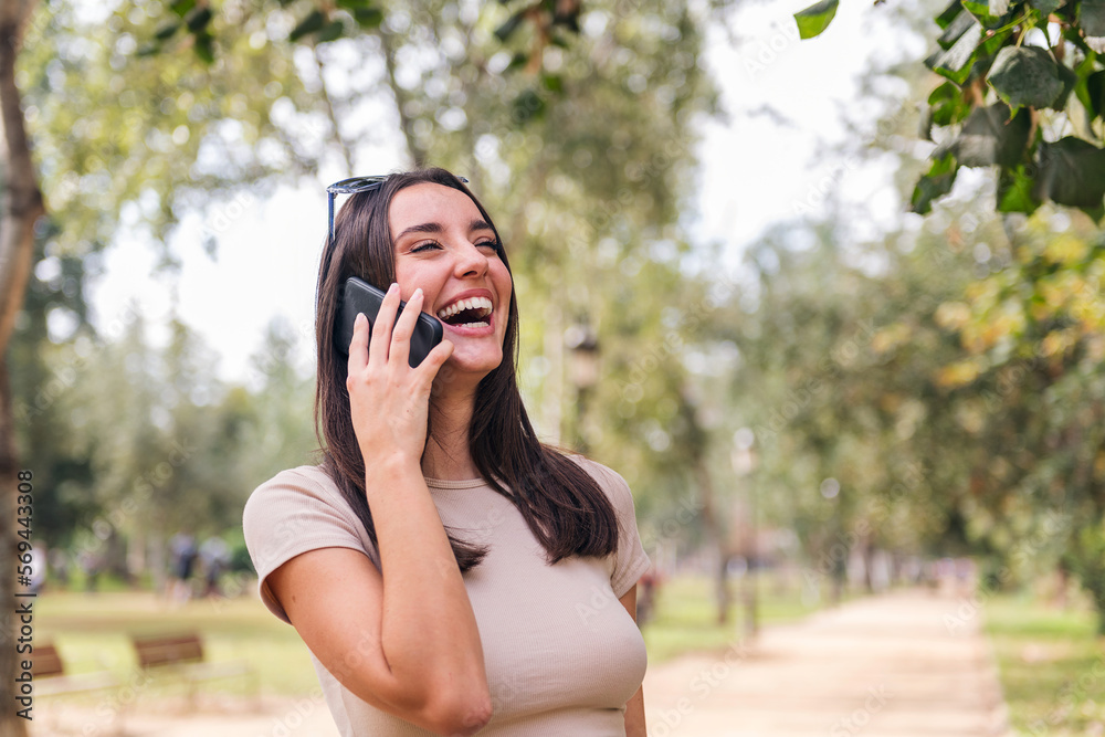 young caucasian woman laughing during a call with her mobile phone in a park, concept of youth and technology of communication, copy space for text young caucasian woman laughing during a call with her mobile phone in a park, concept of youth and technology of communication, copy space for text