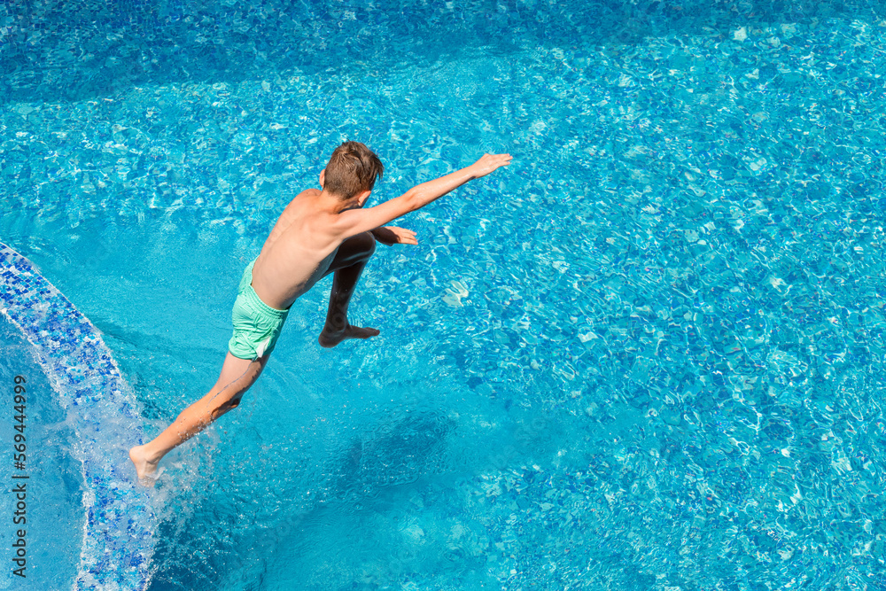 Child boy jumping into blue water of hotel swimming pool. Summer fun, kids sports and wellness activities for children while vacation at resort area. View from above, copy space Child boy jumping into blue water of hotel swimming pool. Summer fun, kids sports and wellness activities for children while vacation at resort area. View from above, copy space