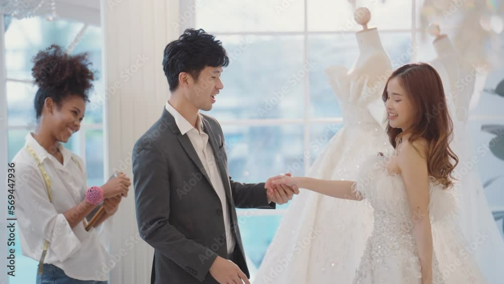 Happy couple bride and groom smiling while choosing and trying to fitting wedding dress for marriage ceremony in bridal shop Happy couple bride and groom smiling while choosing and trying to fitting wedding dress for marriage ceremony in bridal shop
