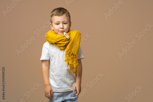 Little sick boy with digital thermometer in mouth on light background. Copy space