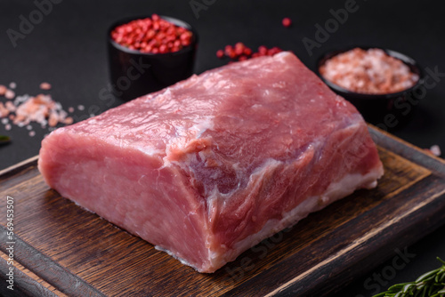 A piece of raw fresh pork on a wooden cutting board with spices and herbs