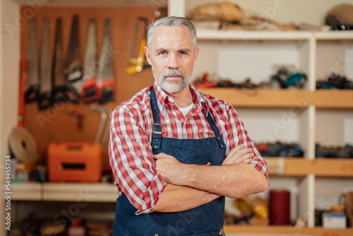 Portrait of professional male carpenter in workshop. Close up of carpenter is posing in a dusty workshop