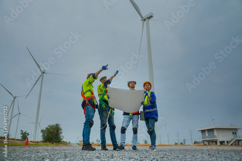 Group of Asian male and female engineer friends holding a blueprint looking at the construction of a turbine power station in a turbine field
