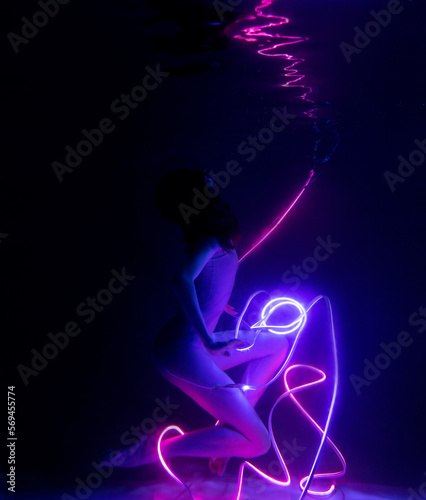 Fototapeta Naklejka Na Ścianę i Meble -  Gymnast shows underwater performance in neon light. Soft blurred focus