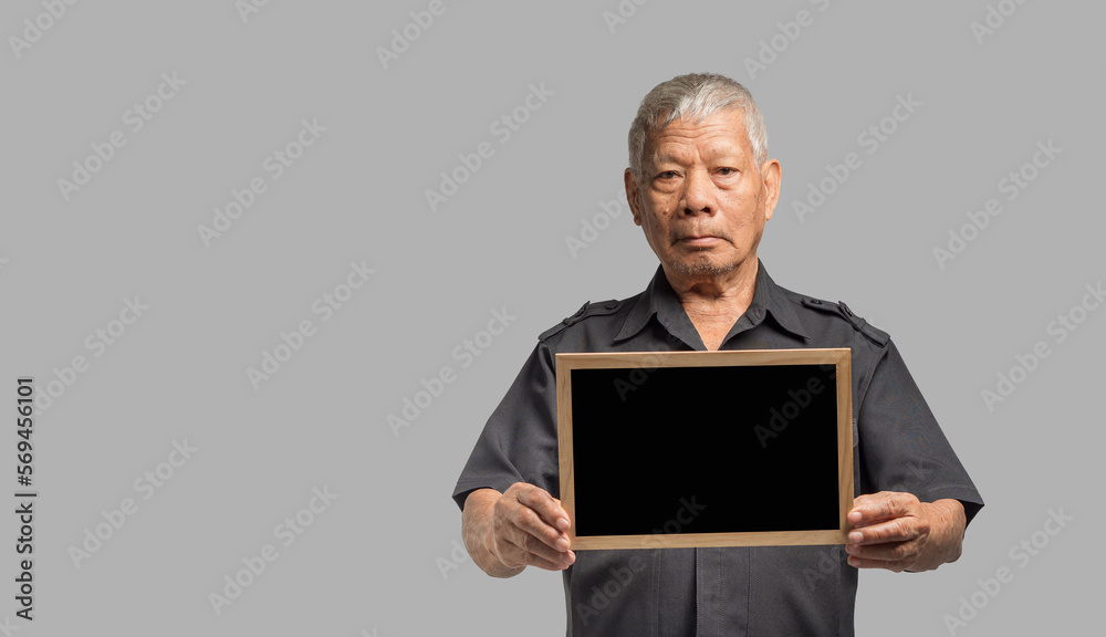 An elderly Asian man holding a mini blackboard and looking at the camera with a smile while standing on a gray background An elderly Asian man holding a mini blackboard and looking at the camera with a smile while standing on a gray background