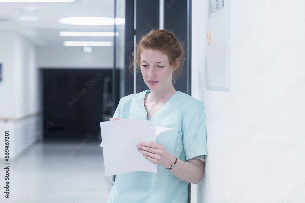Young nurse reading medical charts while leaning  by door