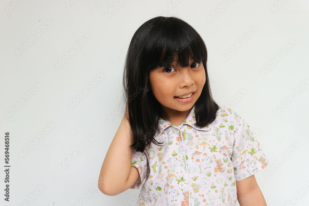 Close-up head shot portrait image with smiling little black-haired girl looking at camera while holding her hair Close-up head shot portrait image with smiling little black-haired girl looking at camera while holding her hair