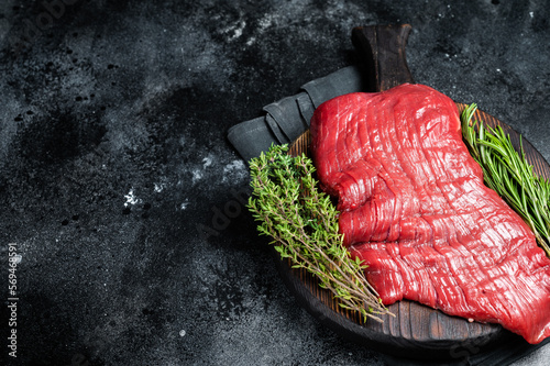 Raw flank beef steak, uncooked meat with herbs. Black background. Top view. Copy space