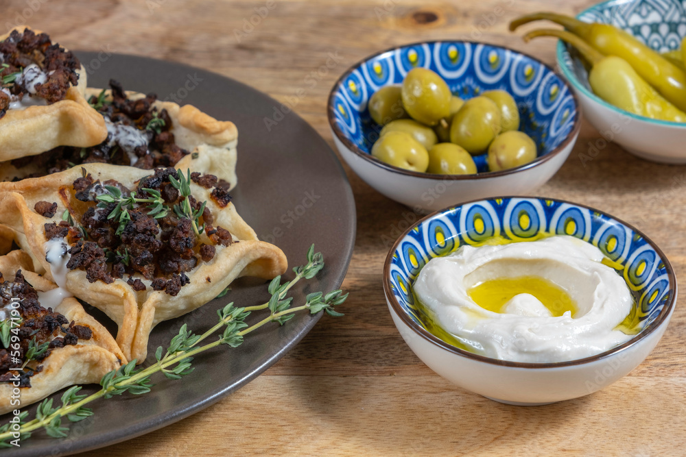 Tahini salad, traditional cookies Hamantaschen with beef meat, fresh thyme and tahini sauce over wooden background.