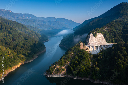 Aerial view of a foggy morning sunrise over a lake and a dam in the mountains next to Siriu Romania  with a cliff road winding