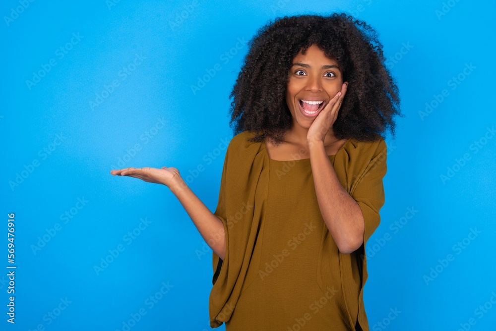 Φωτογραφία Crazy young woman with afro hairstyle wearing brown dress over blue wall advisin