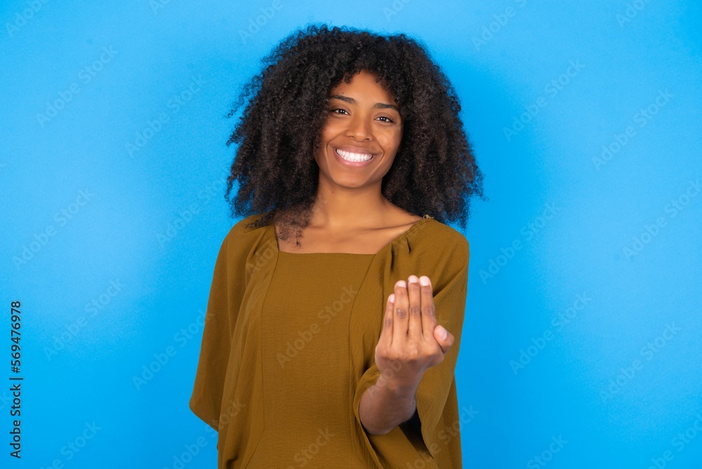 Φωτογραφία young woman with afro hairstyle wearing brown dress over blue wall inviting to come with hand
