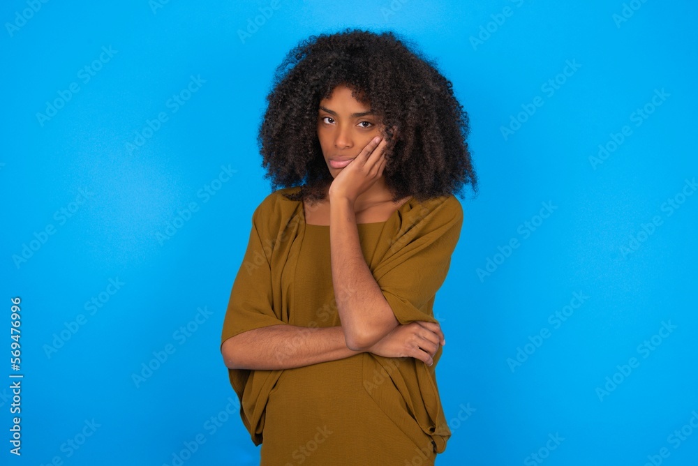 Φωτογραφία Very bored young woman with afro hairstyle wearing brown dress over blue wall ho