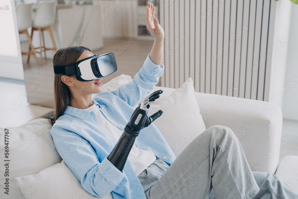Naklejka premium European woman is getting used to modern bionic prosthesis using vr headset. Electronic technology.
