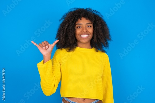young woman with afro hairstyle wearing orange crop top over blue wall showing up number six Liu with fingers gesture in sign Chinese language