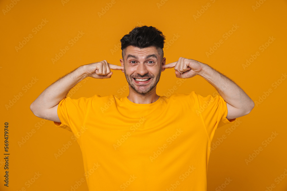 Cheerful guy plugging his ears isolated over yellow background Cheerful guy plugging his ears isolated over yellow background