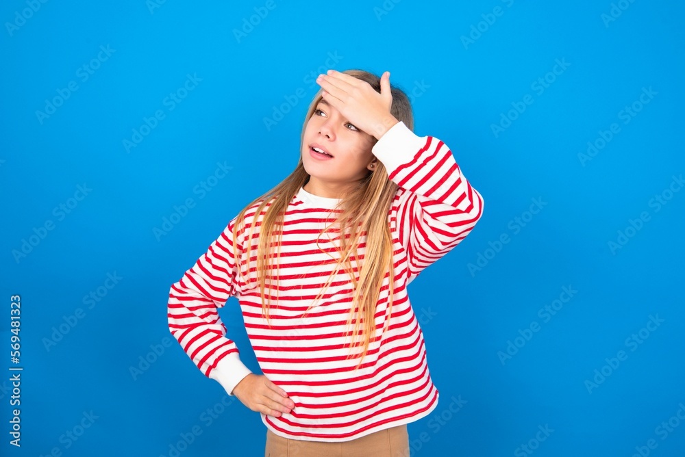 caucasian teen girl wearing striped shirt over blue studio background touching forehead, hears something surprising, glad receive good news, feels relieved. Almost got in trouble. caucasian teen girl wearing striped shirt over blue studio background touching forehead, hears something surprising, glad receive good news, feels relieved. Almost got in trouble.