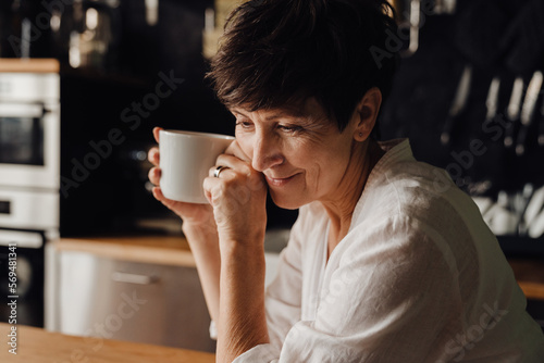Smiling senior woman drinking coffee while sitting in kitchen