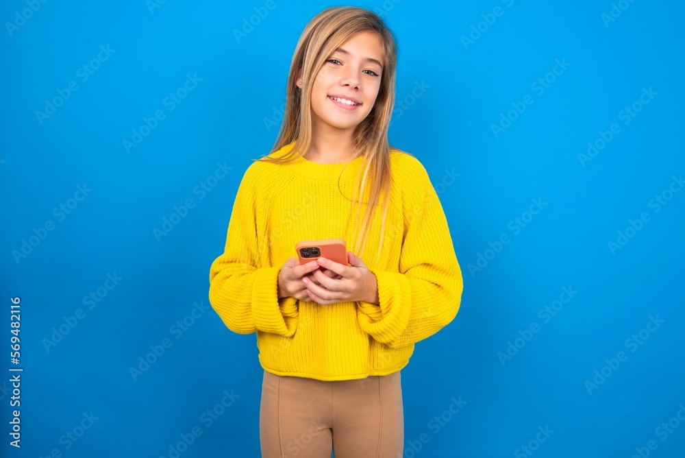 caucasian teen girl wearing yellow sweater over blue studio background Mock up copy space. Using mobile phone, typing sms message caucasian teen girl wearing yellow sweater over blue studio background Mock up copy space. Using mobile phone, typing sms message