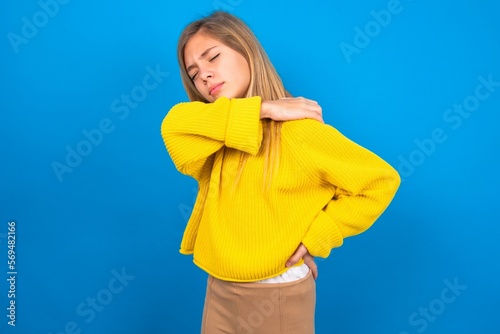 caucasian teen girl wearing yellow sweater over blue studio background got back pain